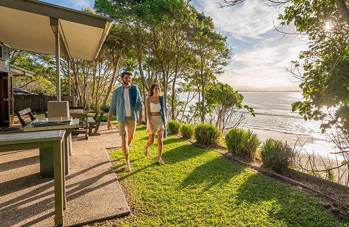 A man an woman walk on grass beside the verandah of Mildenhall Cottage, in Cape Byron State Conservation Area. Photo: John Spencer/DPIE