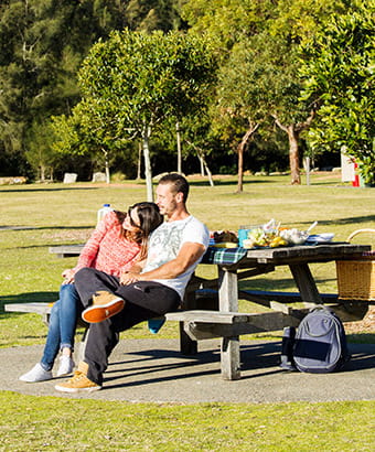 A couple sit together at a picnic table, Bonnie Vale picnic area, Royal National Park. Photo: Simone Cottrell/OEH