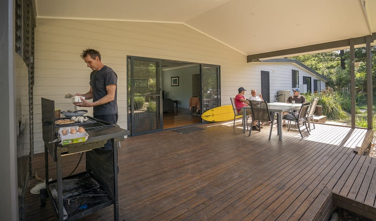 People in the outdoor dining area cooking breakfast on the barbecue and chatting at Plomer Beach House, Limeburners Creek National Park. Photo: John Spencer/OEH